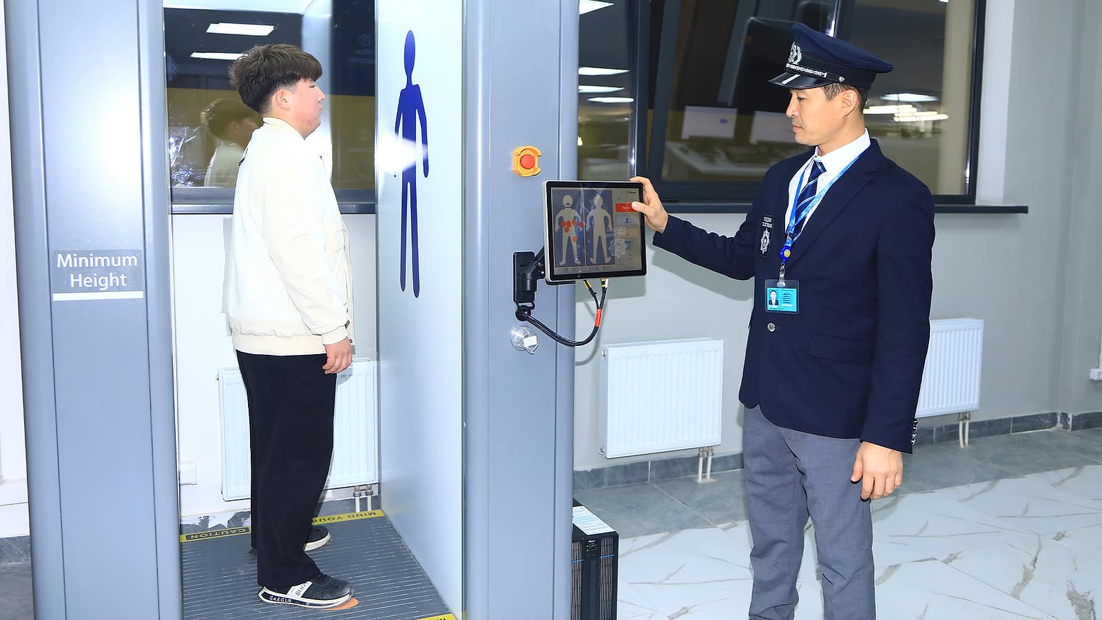 Doganiere kazako in uniforme controlla lo schermo di un body scanner in cui si trova un viaggiatore, a un valico di frontiera