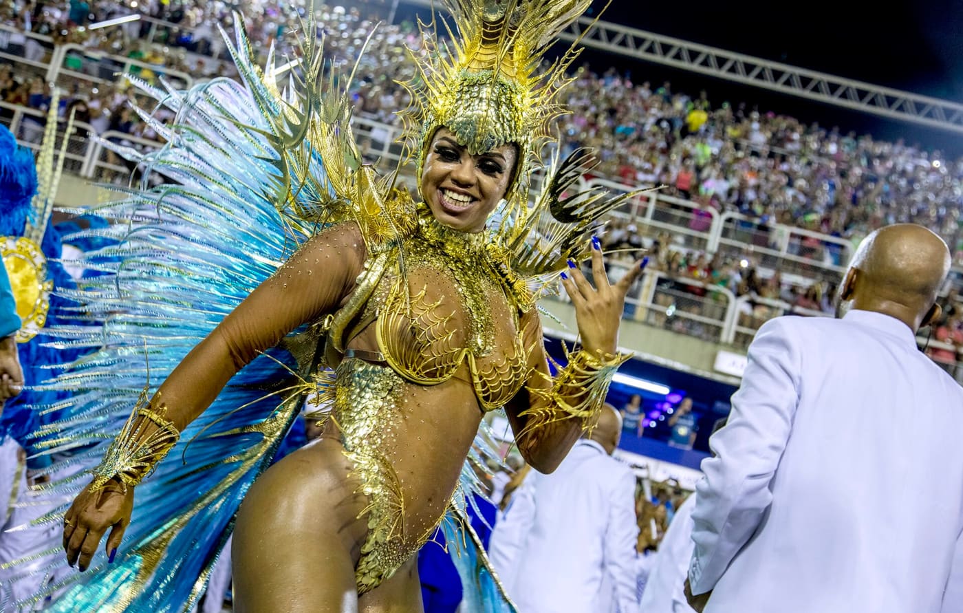 Samba dancer in a gold feathered costume parading the Sambadrome at Rio Carnival, packed stands behind her